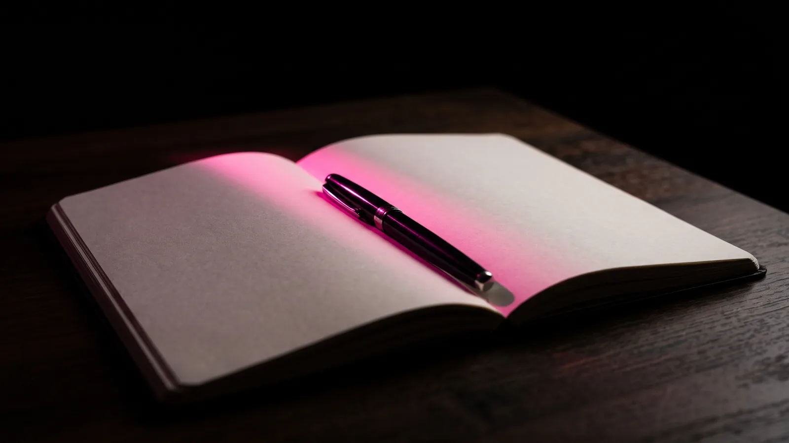 An open blank notebook with a fountain pen across its page on a dark table, lit hot pink, the hiring questions