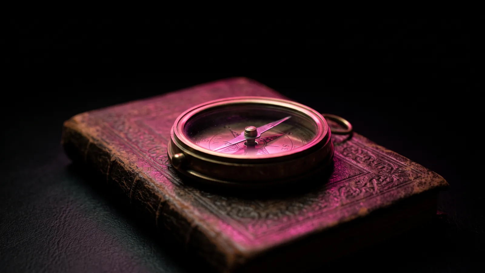 A vintage brass compass resting on a closed leather ledger in darkness, lit only by hot pink light, the direction breach due diligence gives before closing