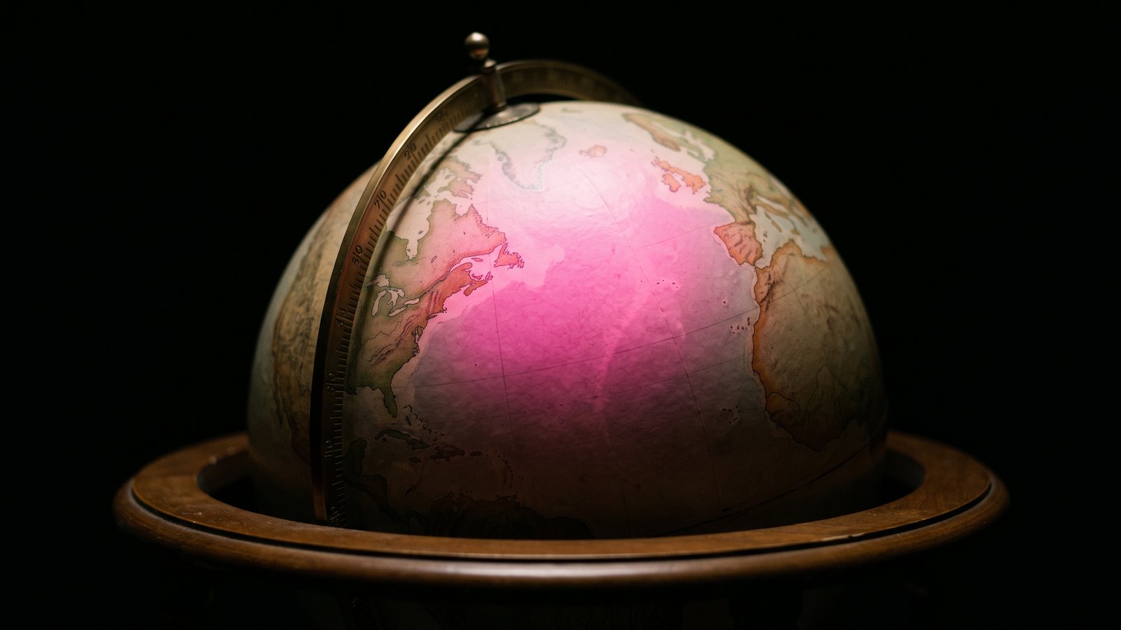 A desk globe in a dark room lit by a single hot pink light falling across the Atlantic between New England and Europe, GDPR for Massachusetts companies