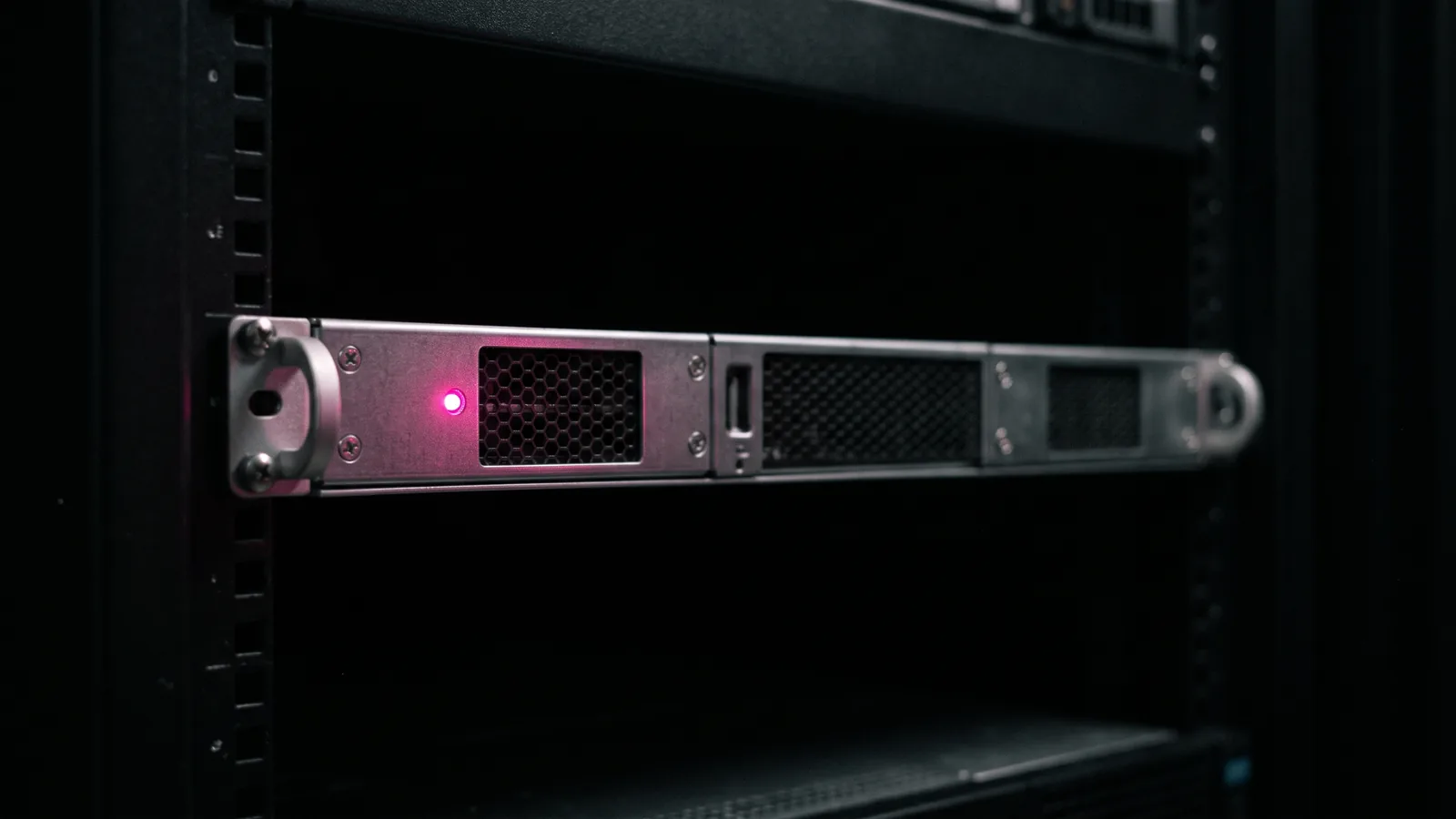 A single rack server in a dark data room with one hot pink status light glowing on its front panel against black