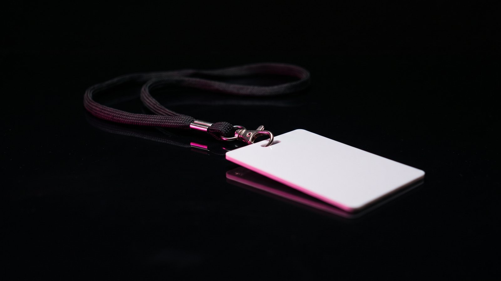 A blank plastic ID badge on a lanyard lying on black glass, its edge lit hot pink, illustrating what is pretexting: a borrowed identity