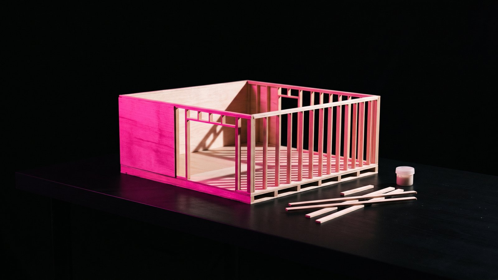 A half-built basswood architectural model in hot pink light on black, the custom website cost for a small business