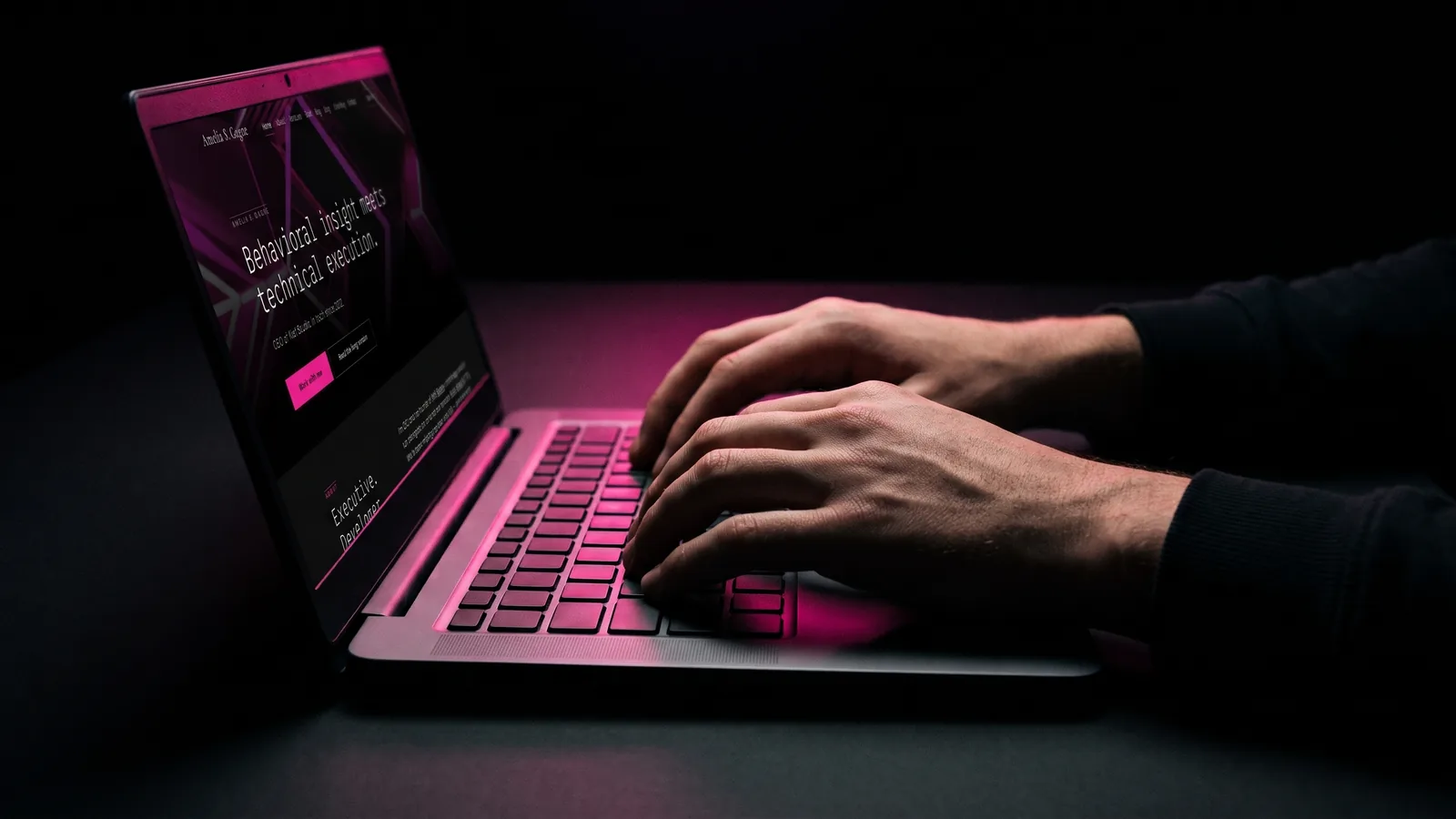 Hands on a laptop keyboard in a dark room, key edges lit hot pink against black, weighing four ways to build a site