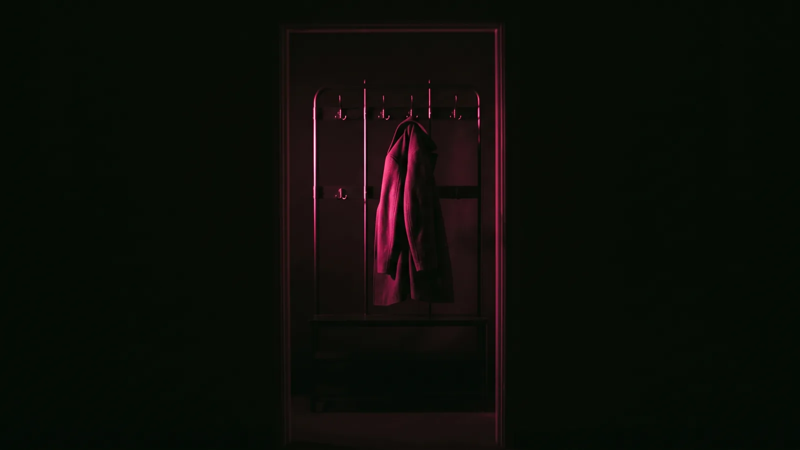 An empty coat rack in a dark entryway with a single coat still hanging, lit by one hot pink light, former admins left on company social media accounts