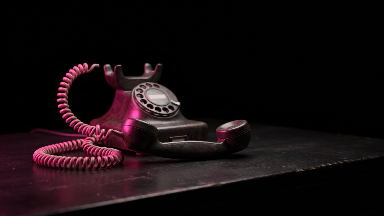 A vintage desk telephone with its handset lifted off the cradle, lit by a single hot pink light against black, for an article on what is vishing